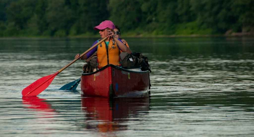 Two people paddle a red canoe on calm water